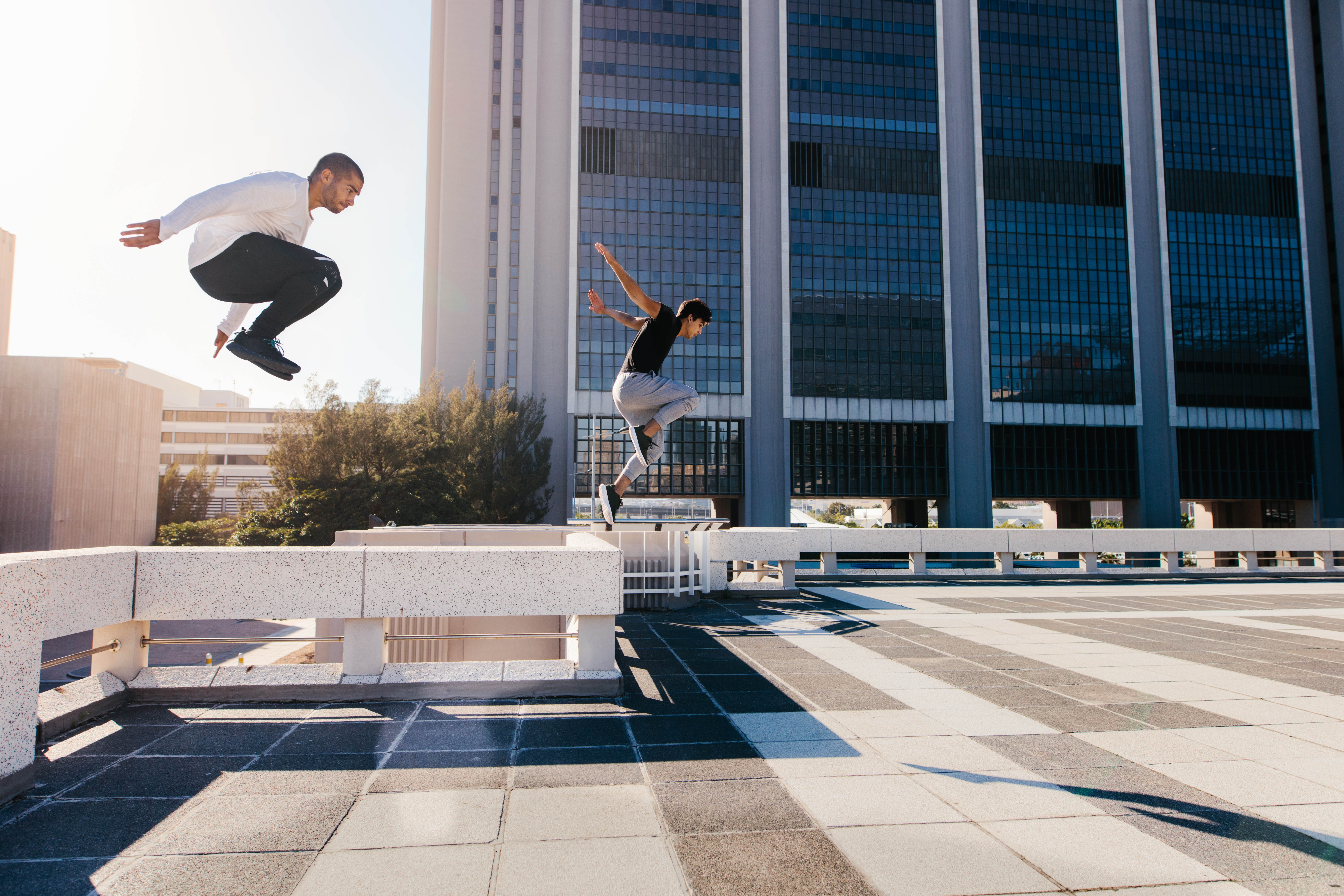 Two young Latino men jumping off of concrete barriers in a city Two young Latino men jumping off of concrete barriers in a city